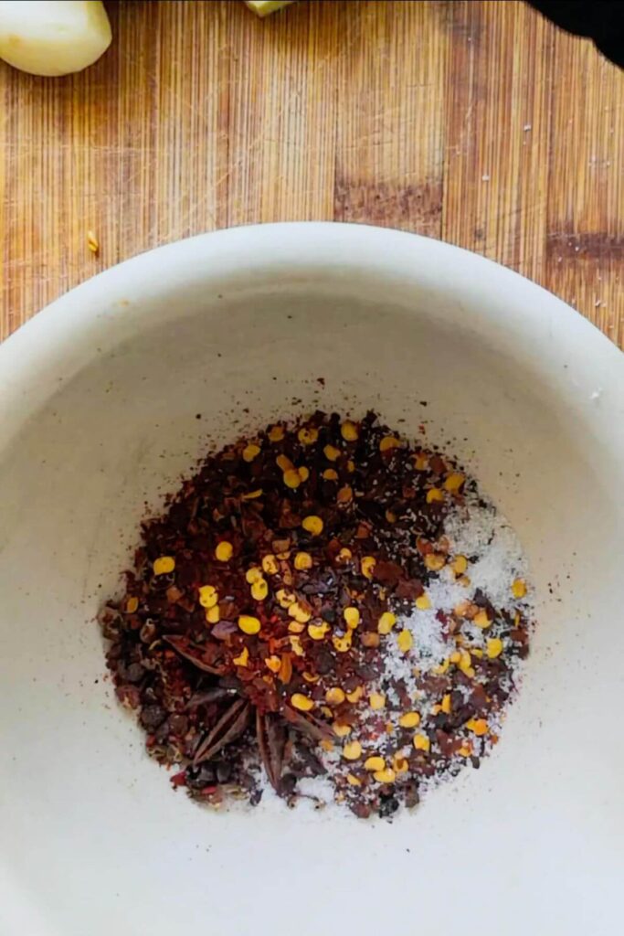 Chilli flakes, star anise, Szechuan peppercorns and salt in a white pestle and mortar.