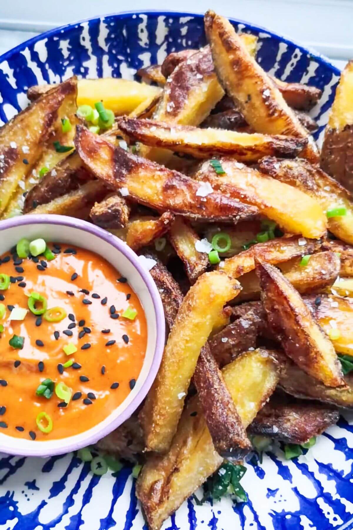 Close up of homemade oven chips in a white and blue bowl with a small pot of spicy gochujang aioli on the side.