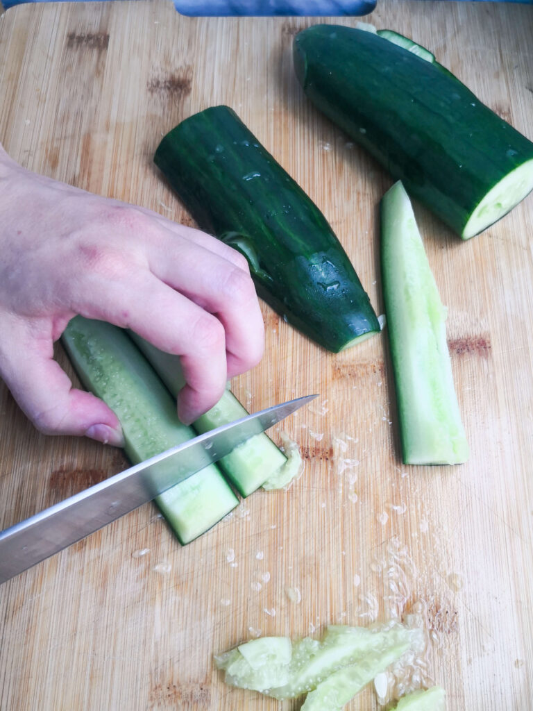 A large silver knife cutting cucumber into small chunks.