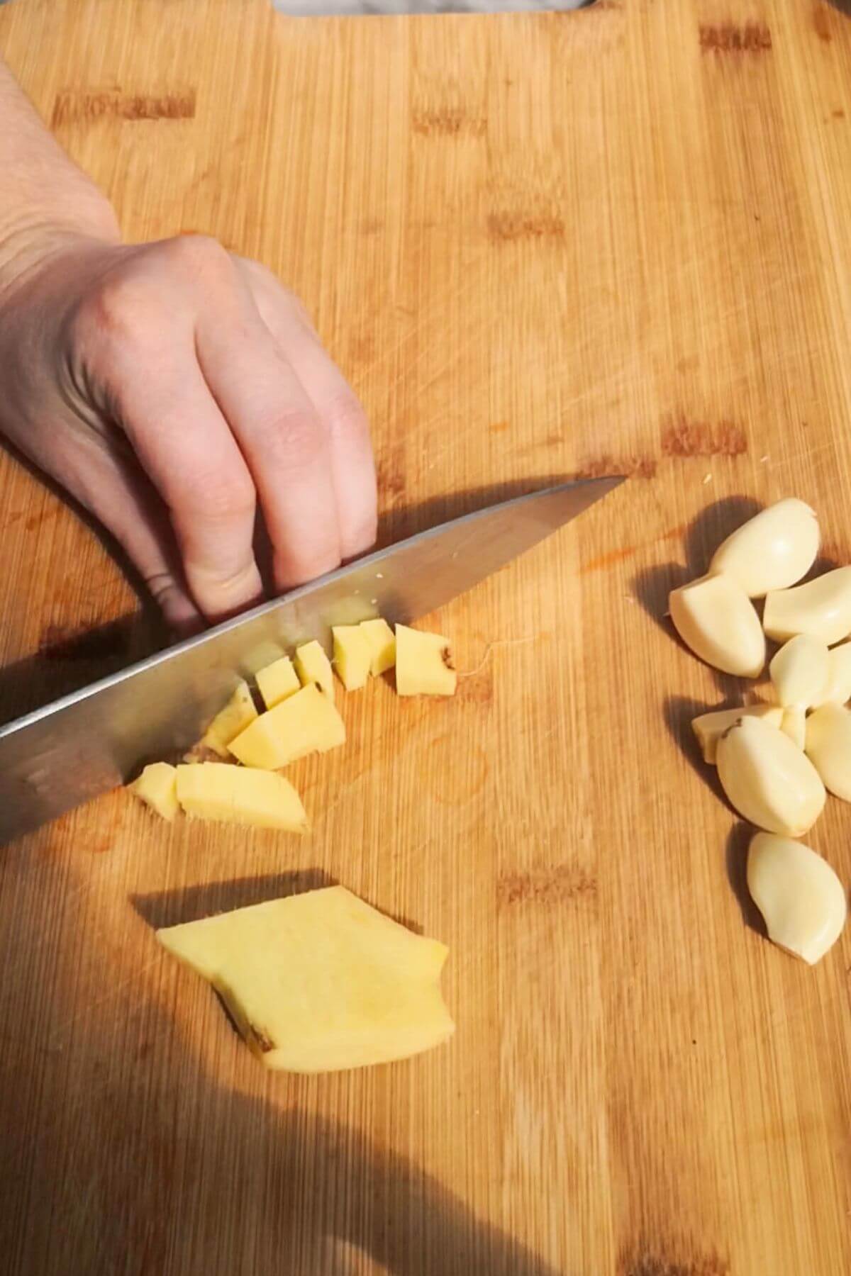 Slicing ginger on a wooden board with a large knife.