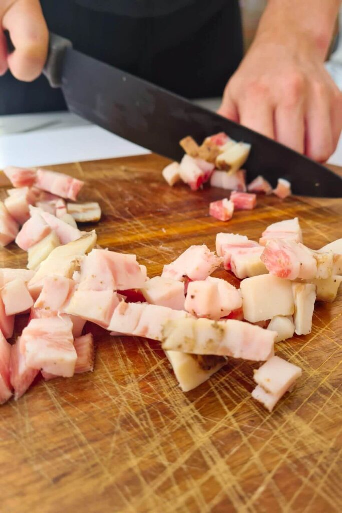 Close up of person dicing guanciale on a wooden board.