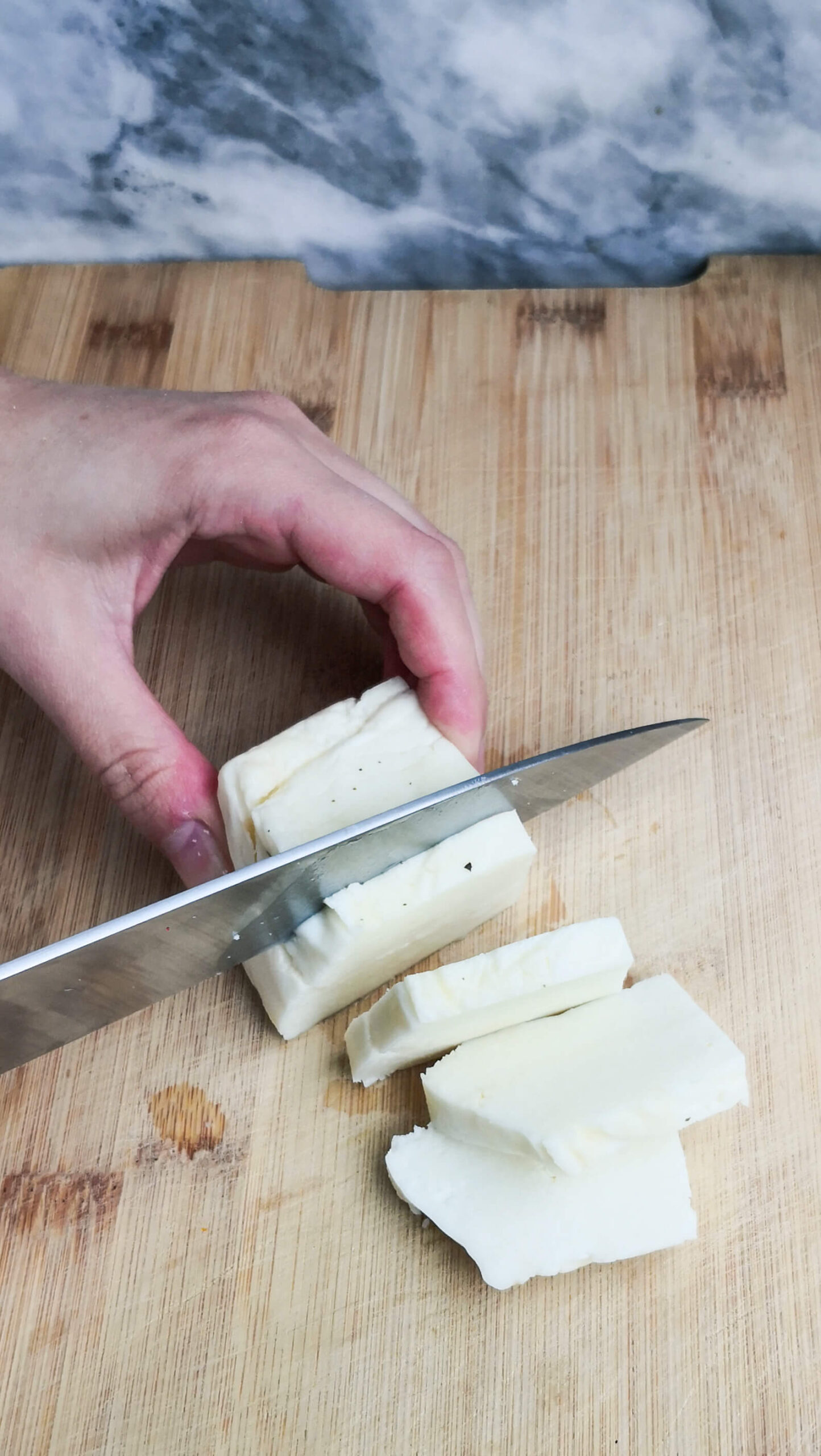 Chopping halloumi into slices on a wooden board.