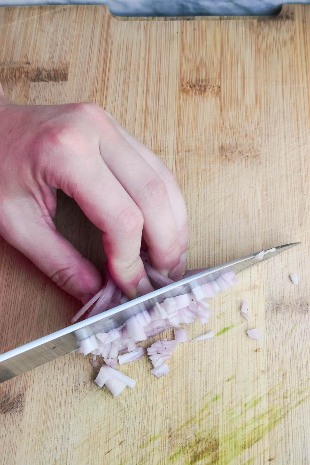 Finely dicing a shallot on a wooden board.