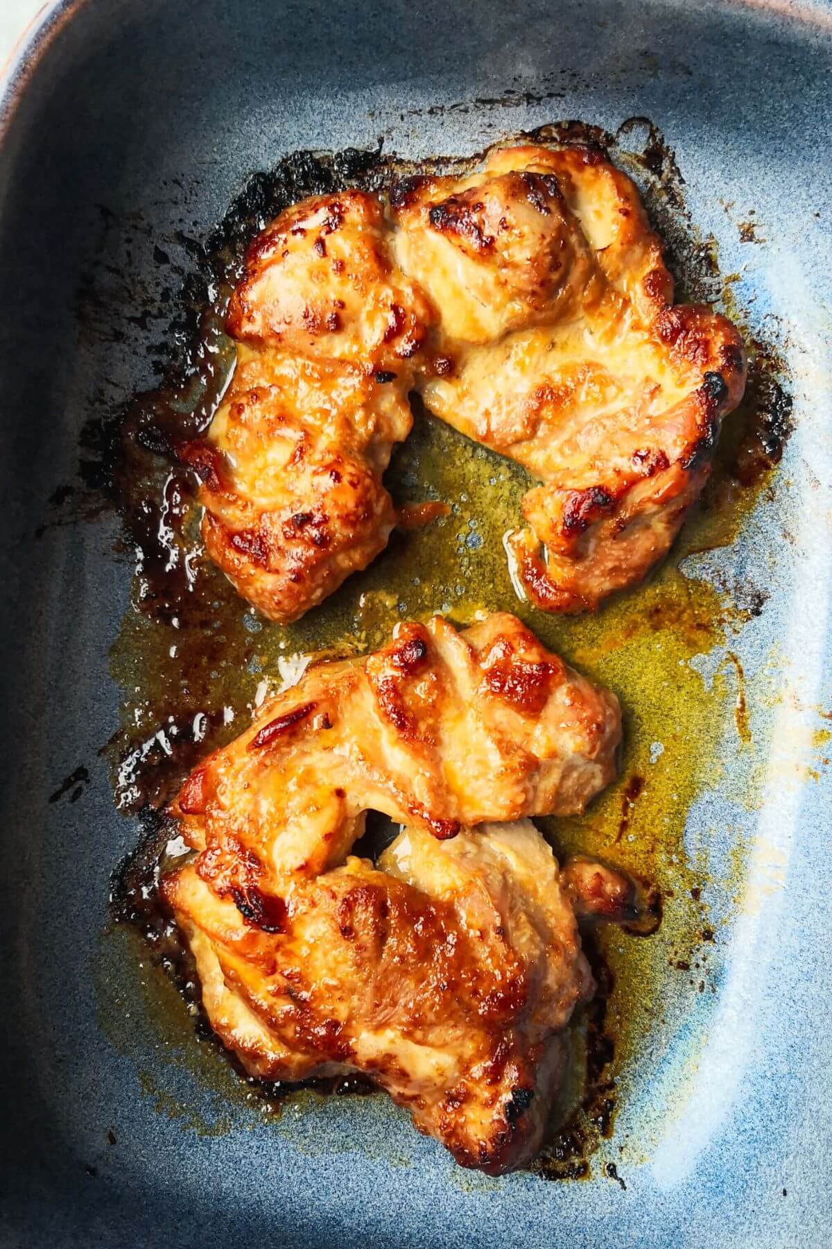 Golden and charred chicken thighs in a small blue oven dish.