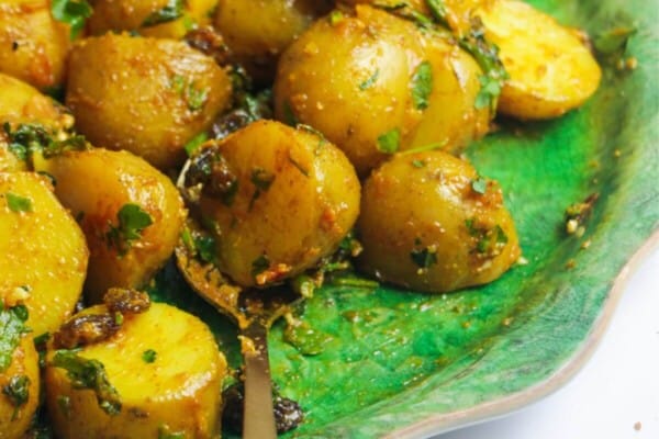 Coronation potato salad on a large green platter with a gold serving spoon and small bowl of coronation sauce on the side.