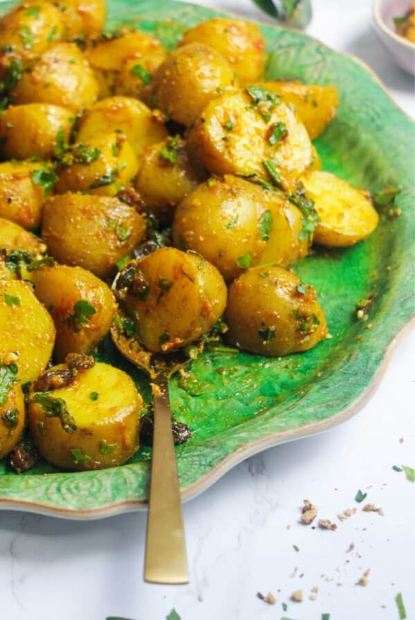 Coronation potato salad on a large green platter with a gold serving spoon and small bowl of coronation sauce on the side.