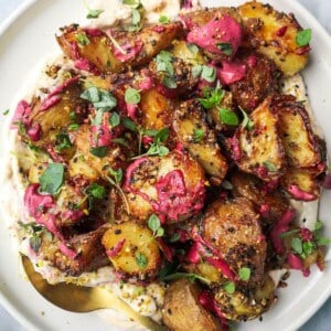 Crispy dukkah potatoes on a bed of aioli with thyme and pink tahini scattered on top.