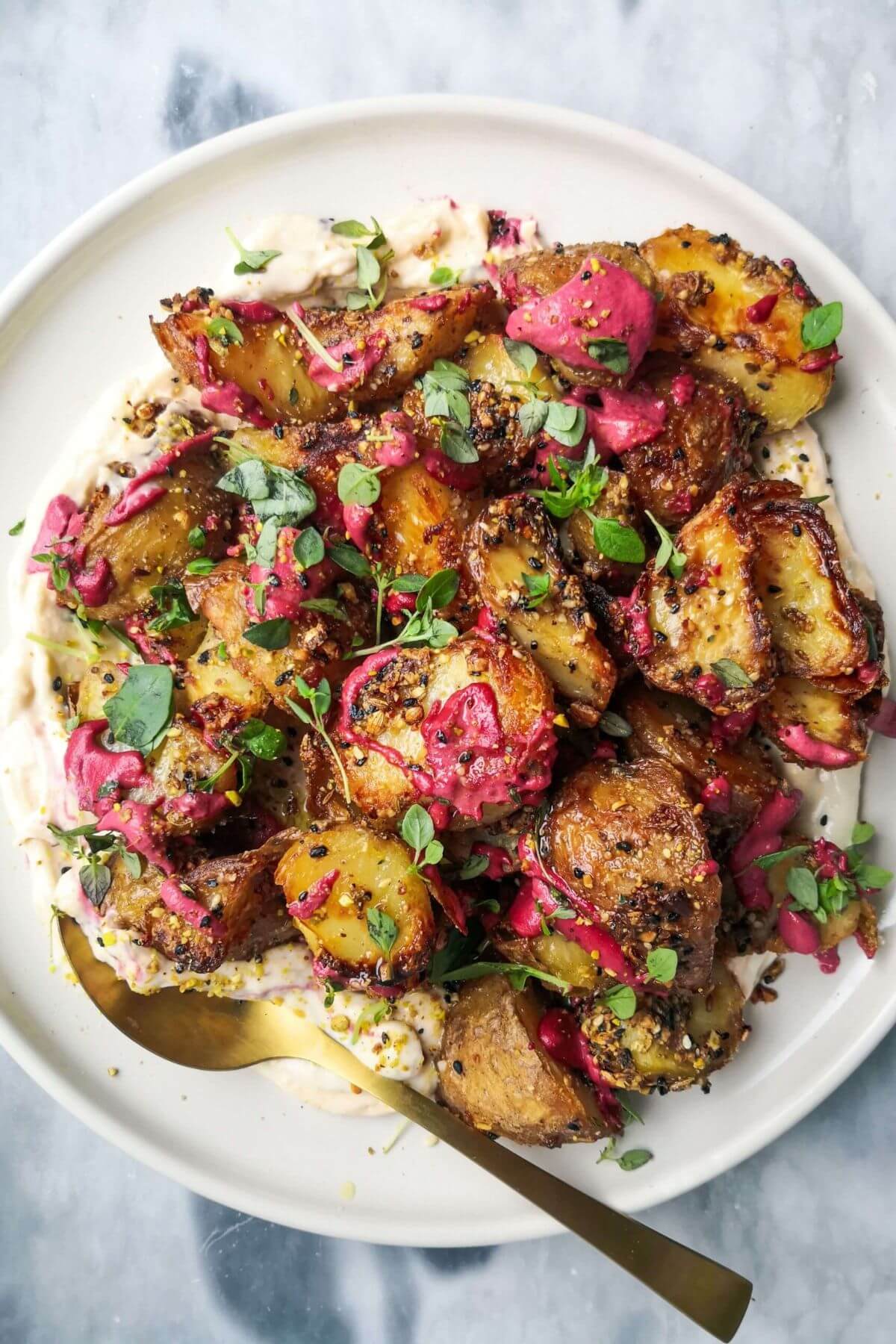 Crispy dukkah potatoes on a bed of aioli with thyme and pink tahini scattered on top.
