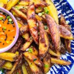 Homemade oven chips with spicy gochujang aioli in a white and blue striped bowl.