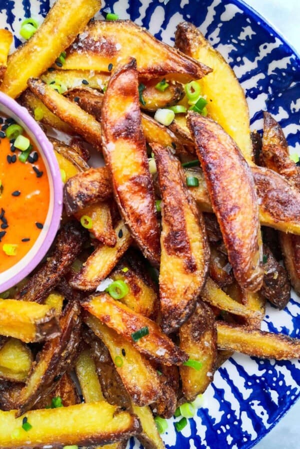Homemade oven chips with spicy gochujang aioli in a white and blue striped bowl.