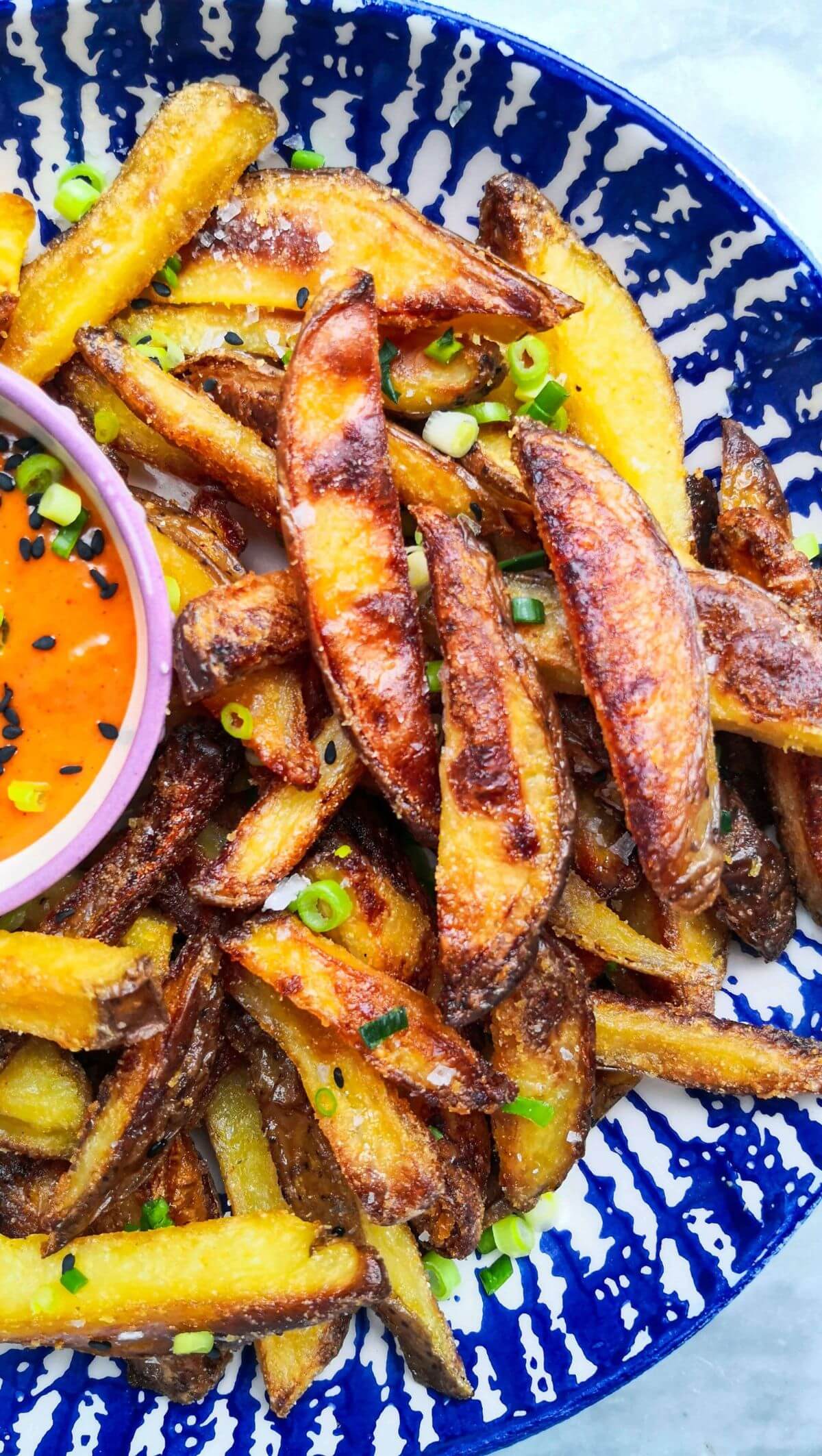 Homemade oven chips with spicy gochujang aioli in a white and blue striped bowl.