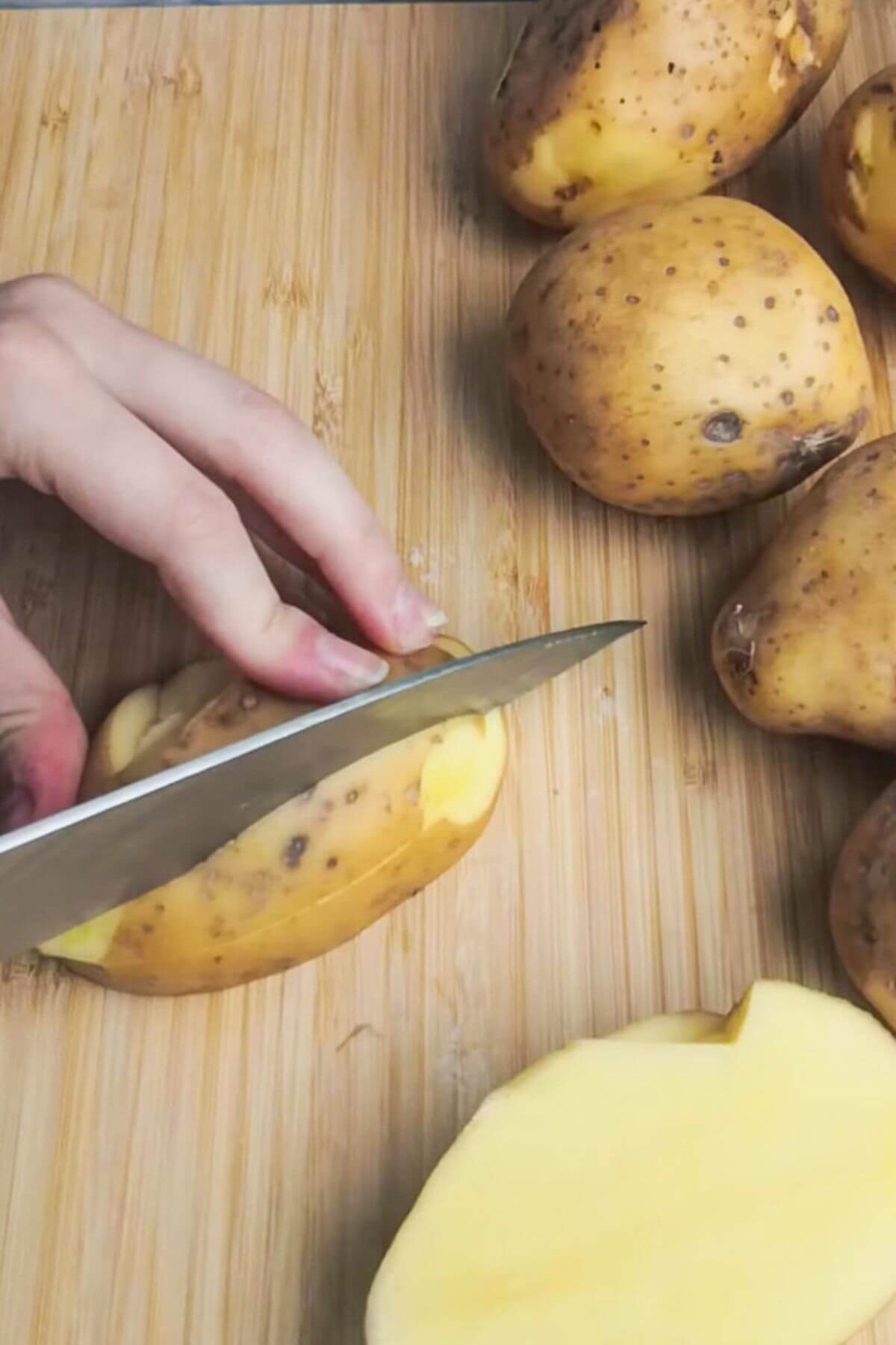 A large knife slicing potato on a wooden board.