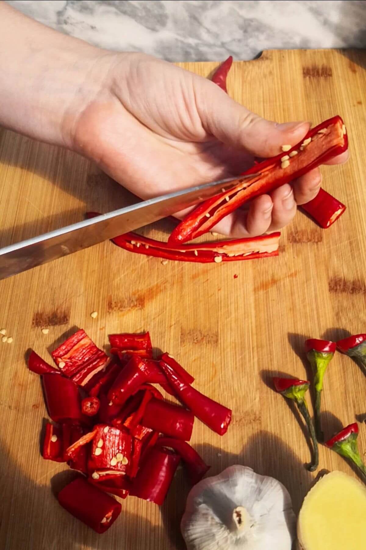 Hand holding a long red chilli with a knife cutting the seeds out of the middle.