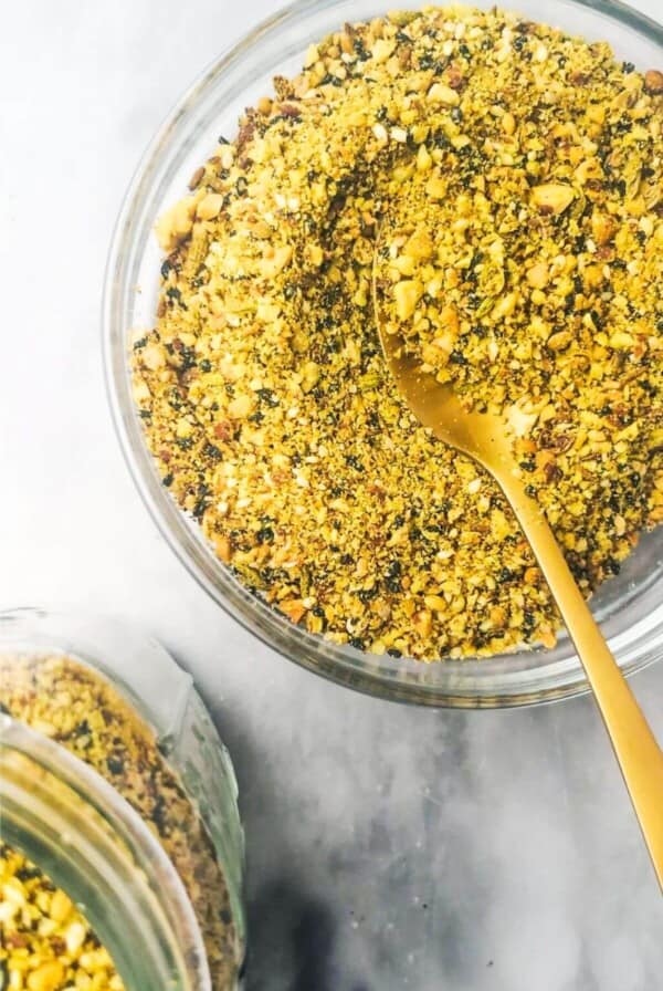 Dukkah in a small glass bowl with a jar on the side.