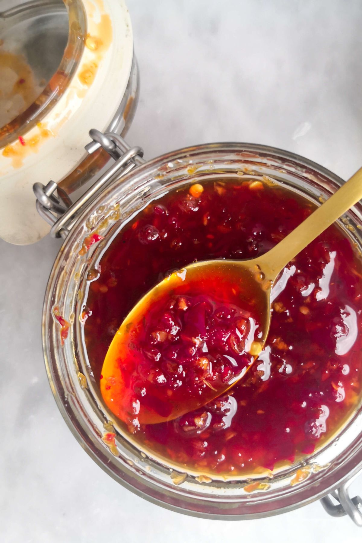 Close up, over head shot of chilli jam in a glass jar, with a gold spoon picking up some jam.