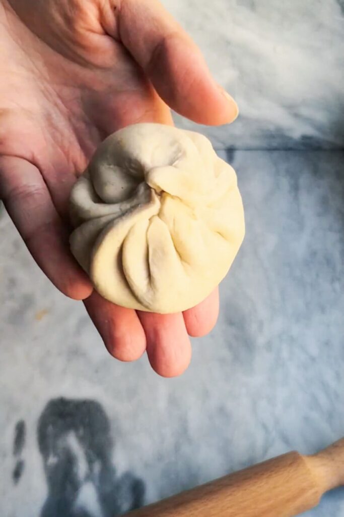 Close up of a sealed steamed bun in a hand.