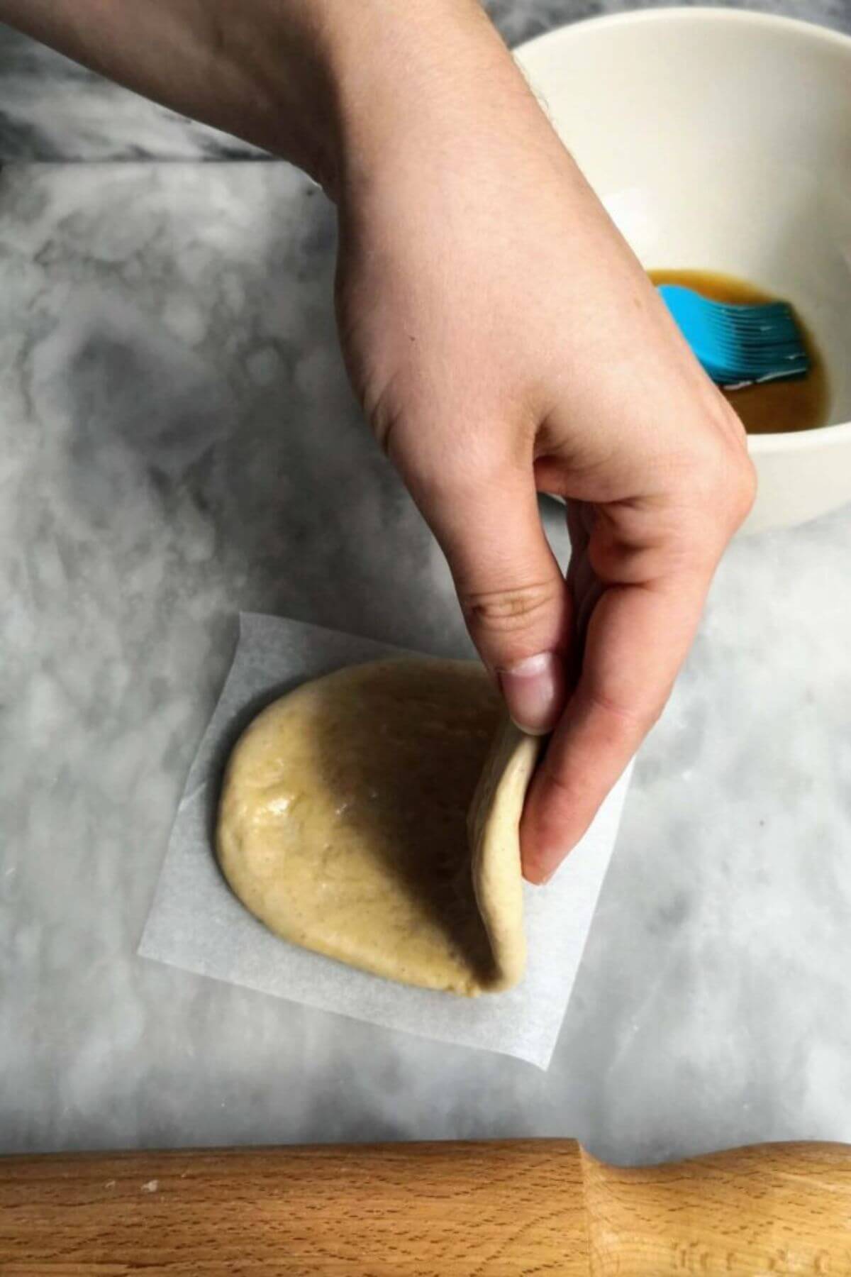 Hand folding over bao bun on a small square of baking paper.