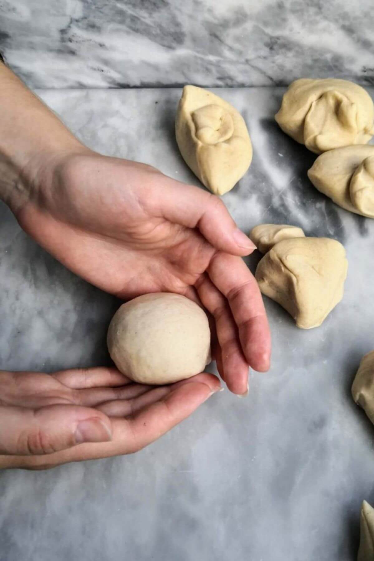 Bao bun dough formed into small balls, being held by hands on a grey marble background.