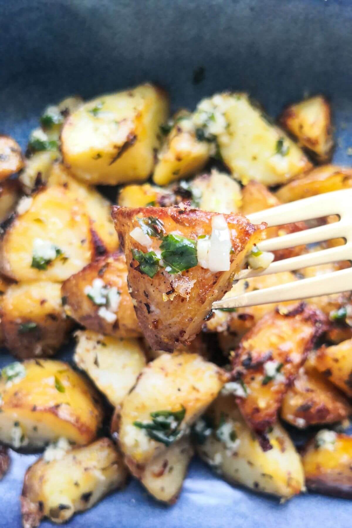 Close up of garlic butter coated potato on a gold fork for more potatoes in the background.