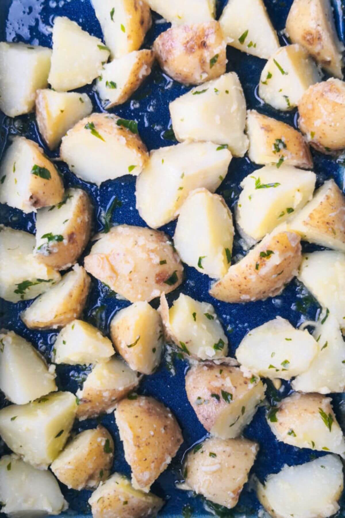 Garlic butter potatoes in a large blue oven dish ready to be roasted.