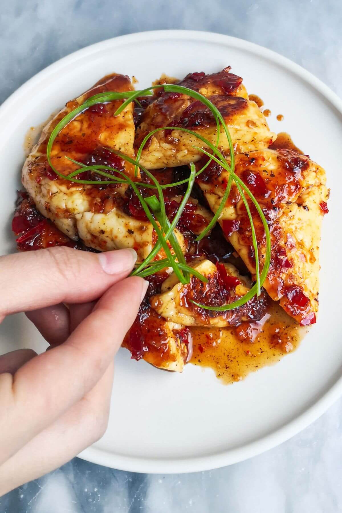 A hand adding curly spring onion to the top of the plate of sweet chilli halloumi.