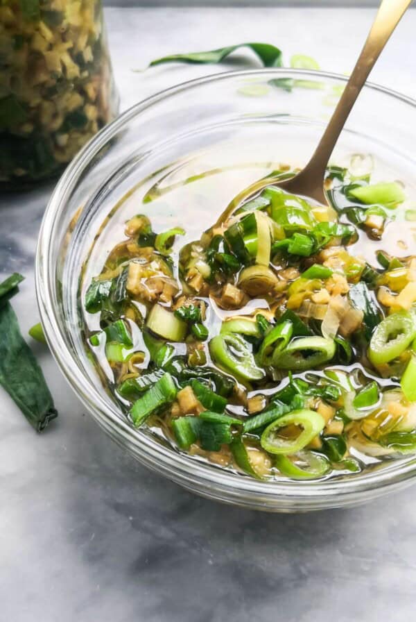 Ginger scallion sauce in a small glass bowl with a gold spoon in it.