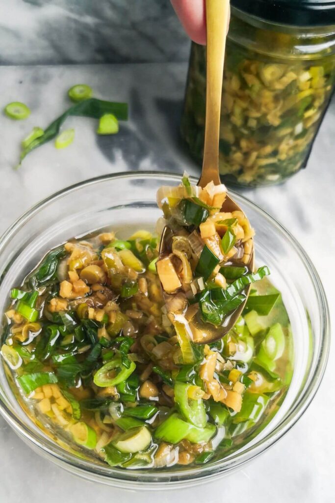 Ginger and spring onion oil in a small glass bowl with a gold spoon stirring through it.