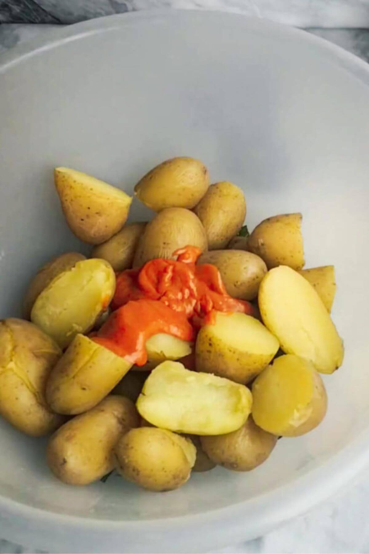 Cooked potatoes and gochujang aioli in a large clear mixing bowl.