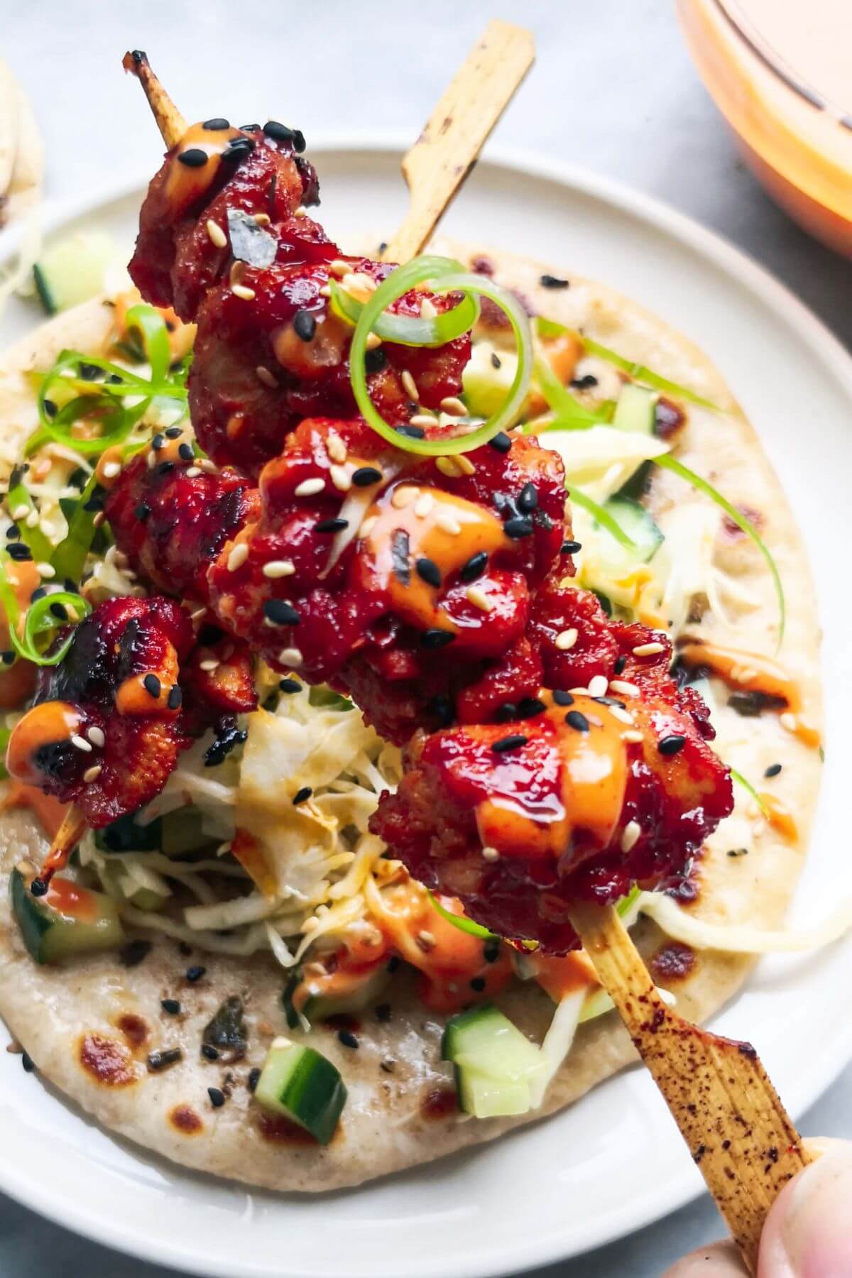 Close up of a gochujang chicken skewer with flatbread and slaw in the background.