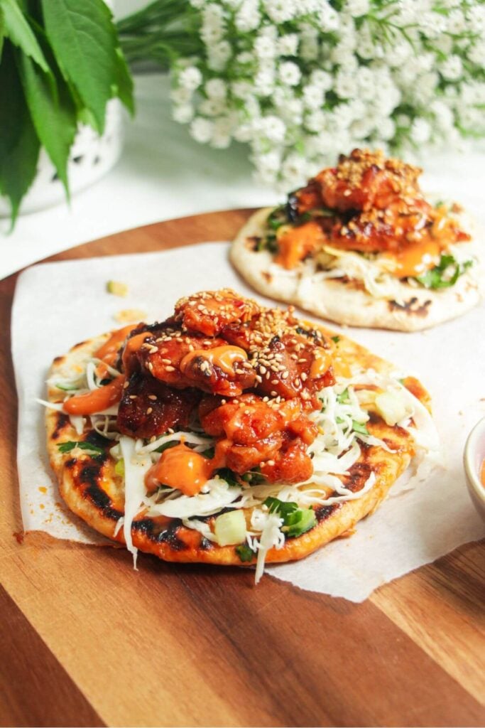 Gochujang chicken on top of slaw on a flatbread on a wooden board.