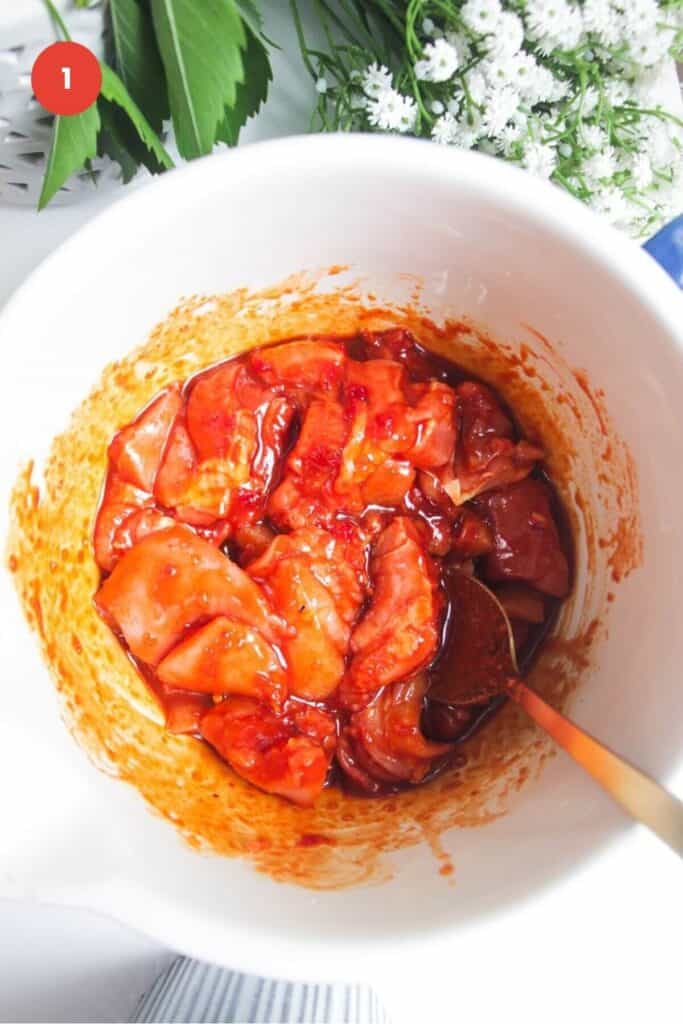 Chicken tossed through gochujang marinade in bowl.