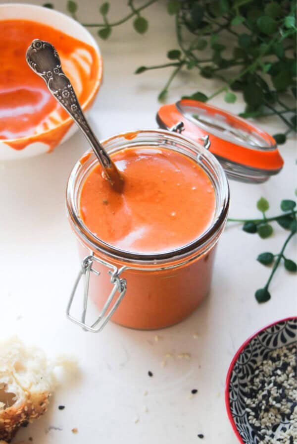 Gochujang mayo in a small glass jar with a bowl of more mayo in the background.