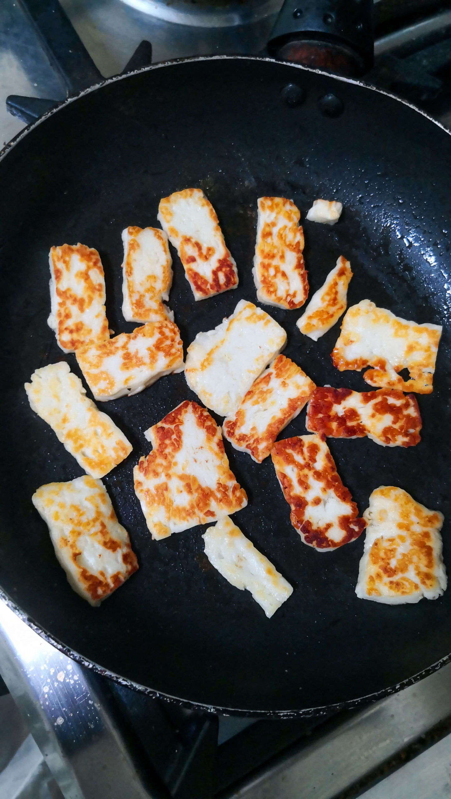 Golden halloumi cooking in a small black pan.