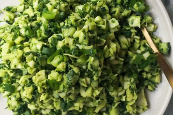 Green goddess salad on a white serving plate with a gold spoon, with green goddess dressing in a small bowl on the side.