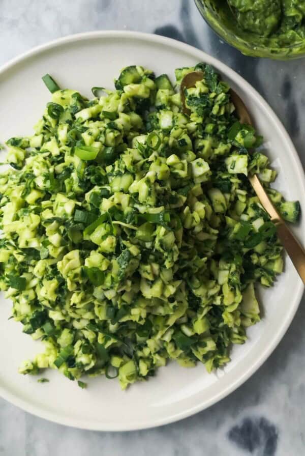 Green goddess salad on a white serving plate with a gold spoon, with green goddess dressing in a small bowl on the side.