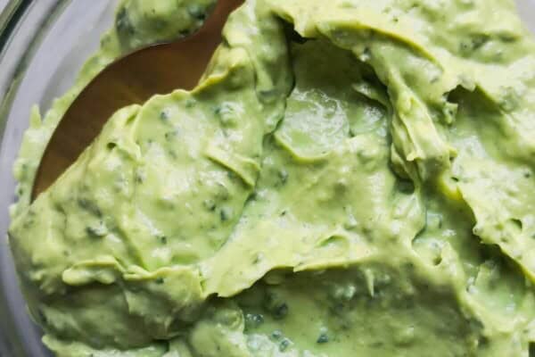 Green tahini sauce in a small glass bowl with a gold spoon inside, on a grey marble background.