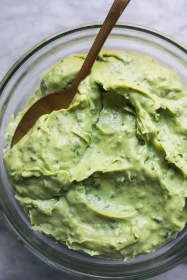 Green tahini sauce in a small glass bowl with a gold spoon inside, on a grey marble background.