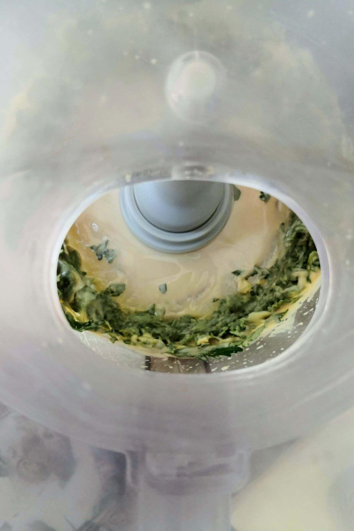 Green tahini being blitzed in the bowl of a food processor.