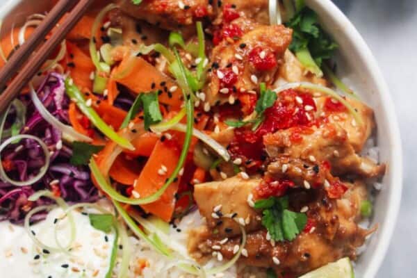 Chicken poke bowl on a grey marble background, with chopsticks on the side and a jar of dressing.