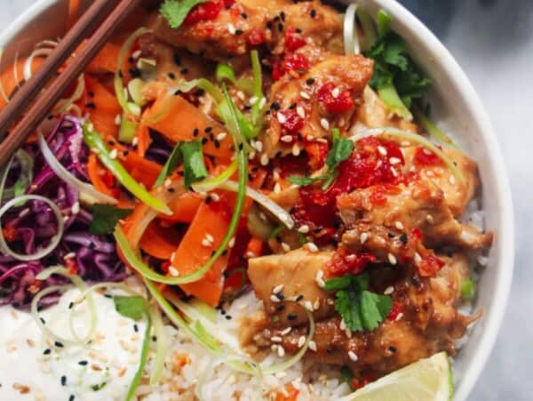 Chicken poke bowl on a grey marble background, with chopsticks on the side and a jar of dressing.