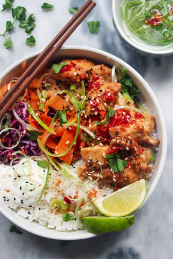 Chicken poke bowl on a grey marble background, with chopsticks on the side and a jar of dressing.