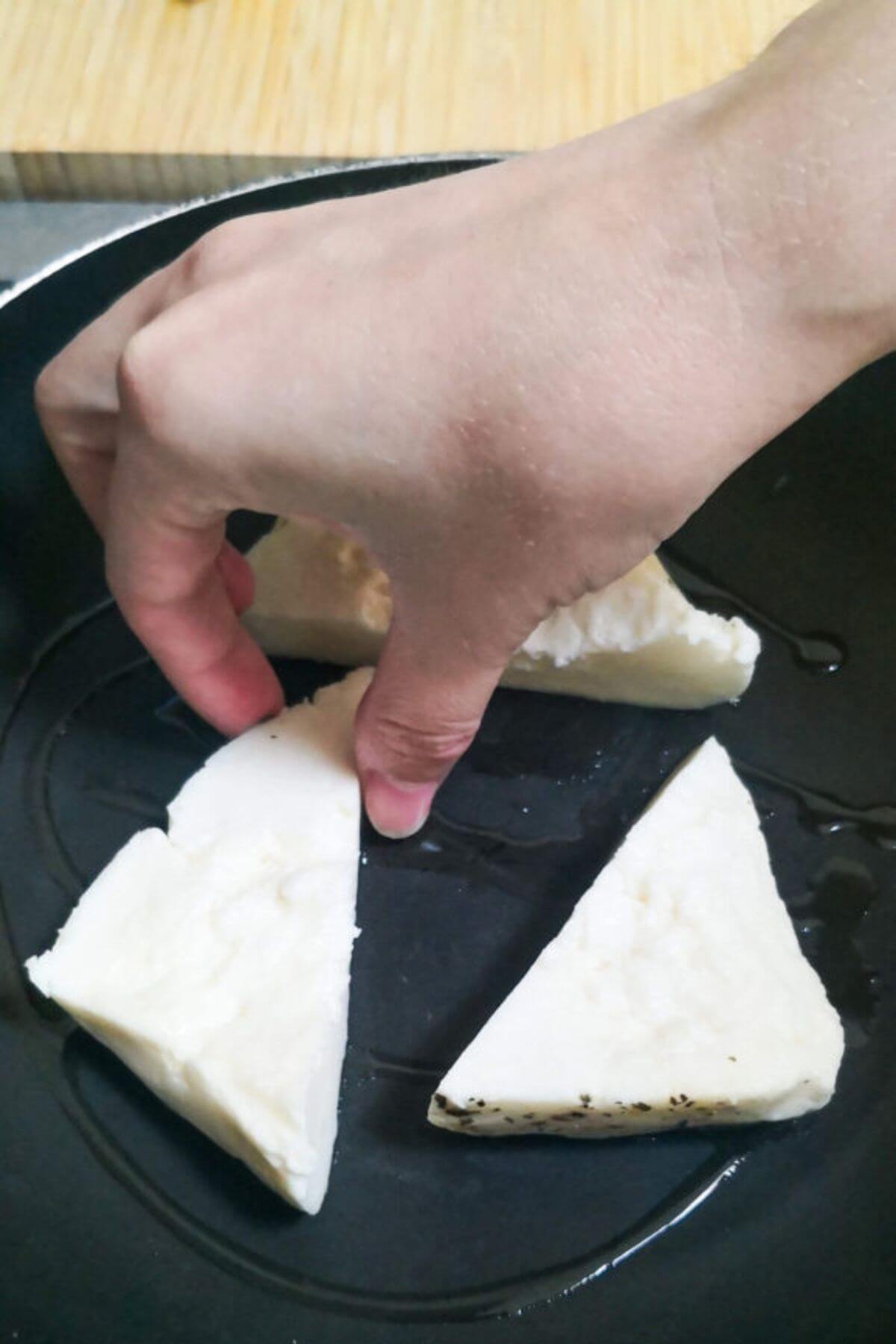 A hand placing halloumi triangles in a small black pan.