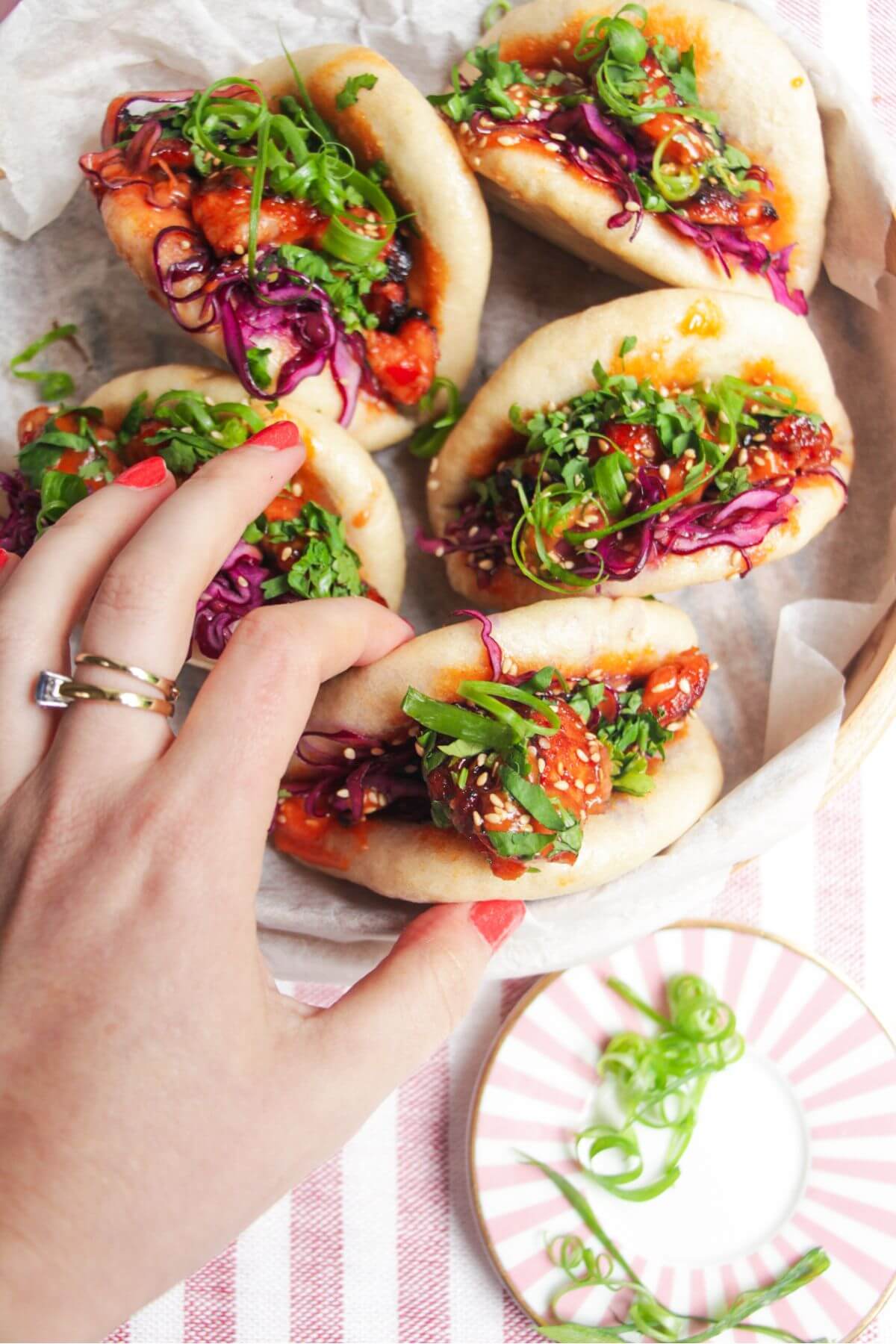 Five Korean chicken filled bao buns on a pink plate with aioli on the side.