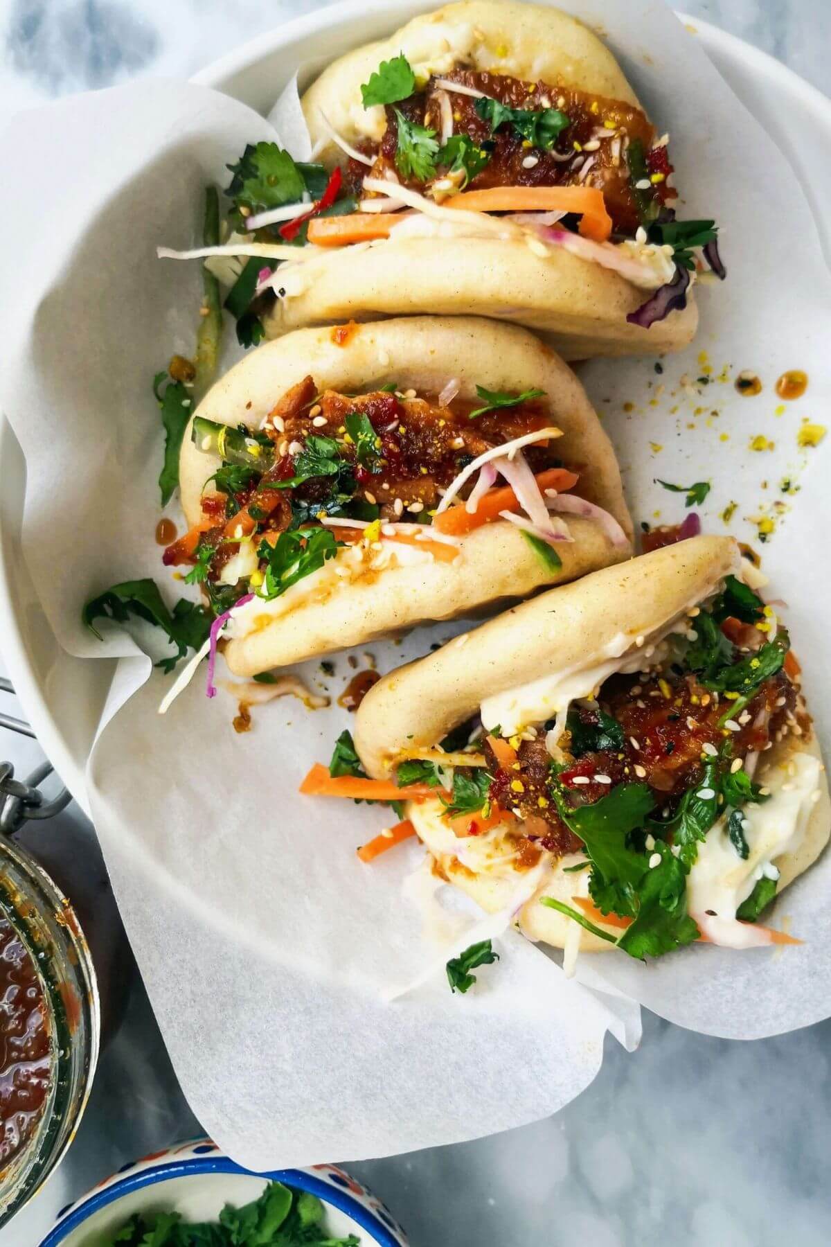 3 bao buns in a small white bowl with chilli jam on the side.