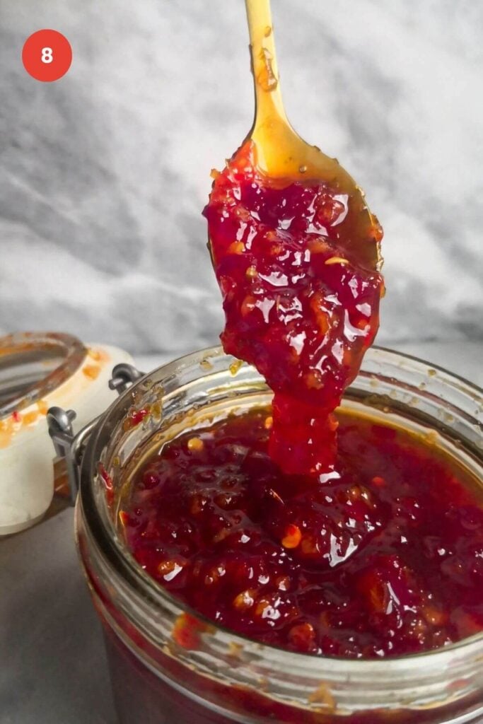 Spooning thickened chili jam into a jar.