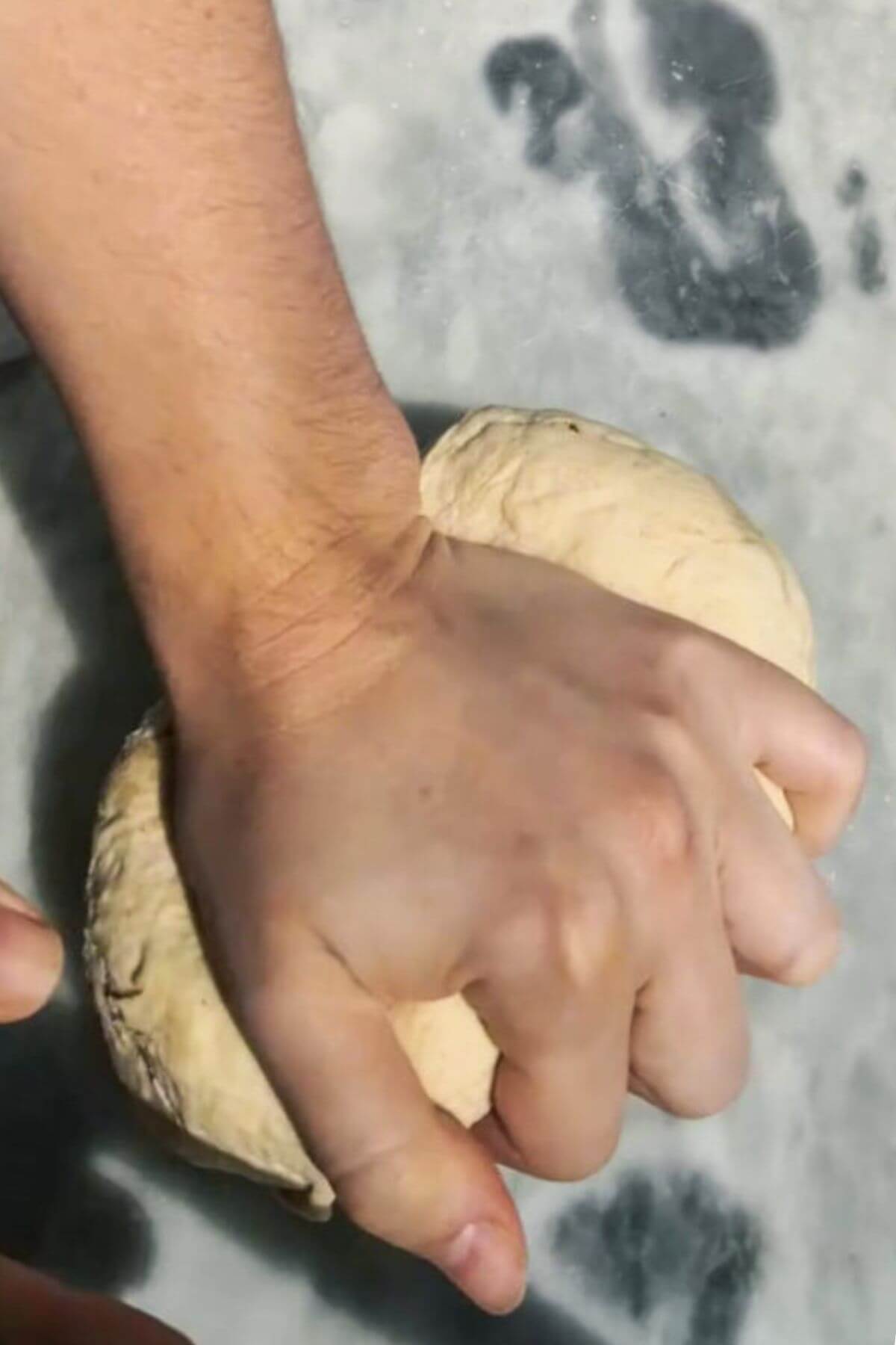 Hand kneading bao bun dough on a grey marble background.