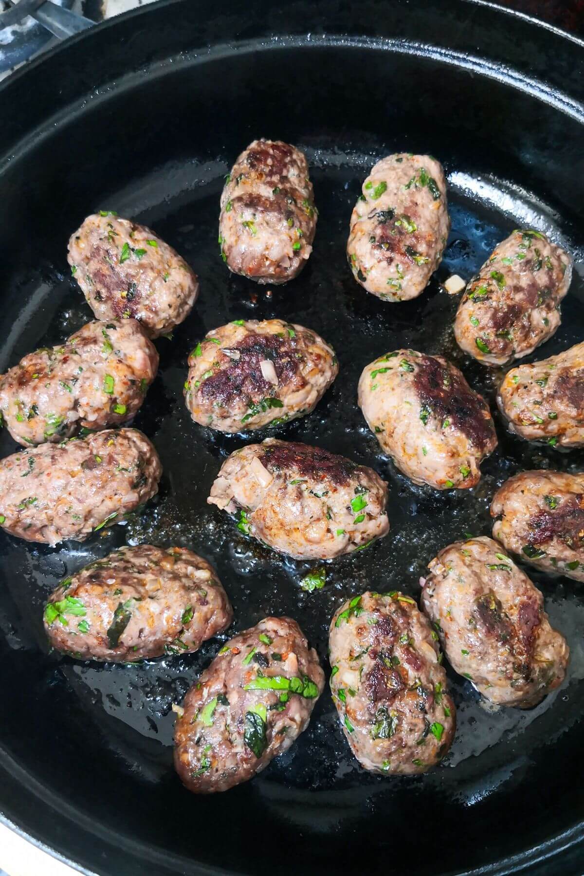 Browned lamb kofta cooking in a black skillet on the stove top.