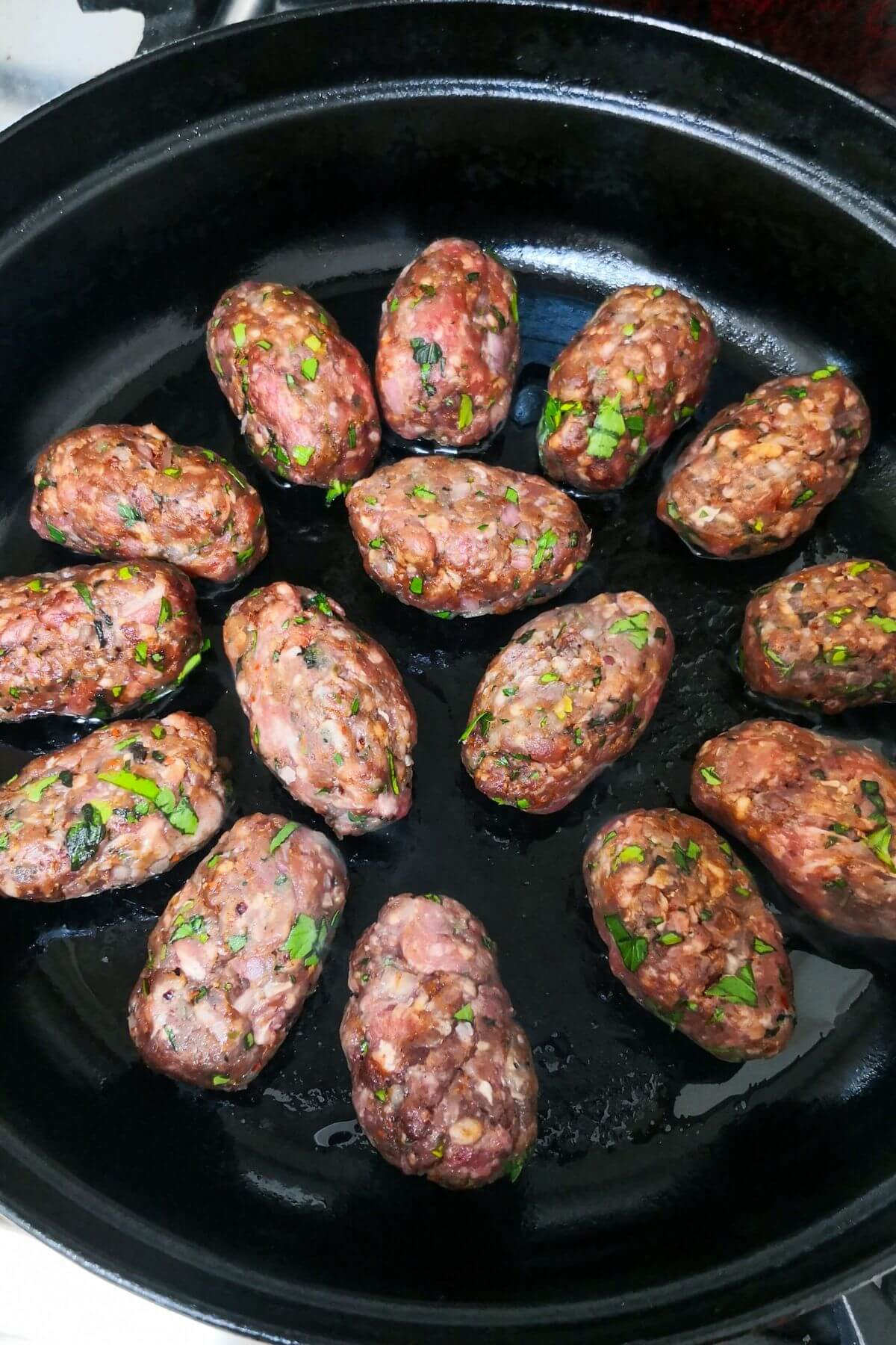 Lamb kofta cooking in a black skillet on the stove.