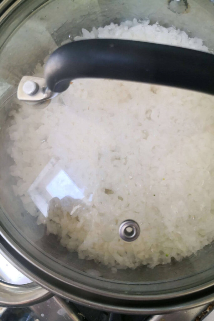 Clear lid with a black handle covering the pot of sushi rice cooking on the stove top.