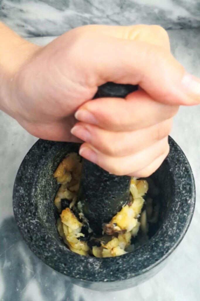 Hand mashing roasted garlic into a paste in a pestle and mortar.